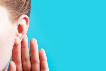 Girl listens attentively with her palm to her ear close-up on a blue background.