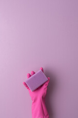 A hand in a pink protective rubber glove holds a washing sponge on a purple background