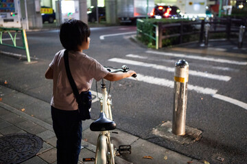 夜道で信号待ちをする自転車を押した女の子 - obrazy, fototapety, plakaty