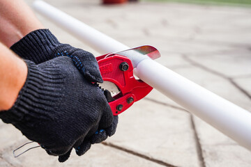 The hands of the foreman hold metal scissors for cutting plastic water pipes outside.
