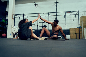 Fototapeta na wymiar Mixed race friends doing cross fit in the gym. Male personal trainer giving African American female a high-five after exercising. High quality photo