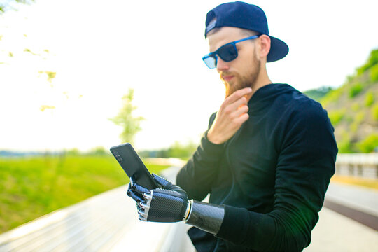 young bearded man with metal arm prosthetic outdoor looking at screen of smartphone