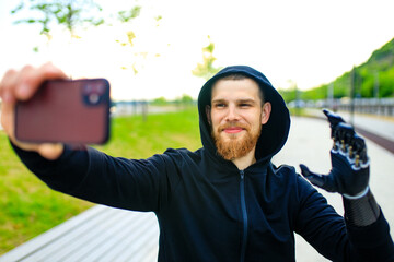 young bearded man with metal arm prosthetic outdoor taking selfie photos on smartphone camera