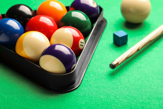 Billiard balls in triangle rack, cue and chalk on green table, closeup