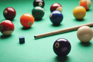 Many colorful billiard balls, cue and chalk on green table