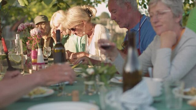 group of seniors friends people sitting outdoors having lunch or dinner together toasting and laughing - good quality time in the third age concept