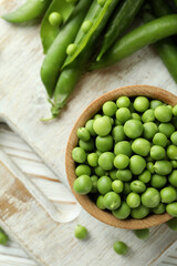 Bowl with pea seeds and fresh pea on wooden background