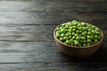 Bowl with pea seeds on wooden background