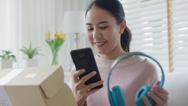 Young asia people happy teen girl smile unbox open gift new headphone buy order from online store shop take photo shoot camera show post social media app blog vlog share sit relax at home sofa couch.