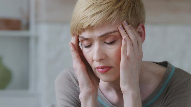Face of upset unhappy depressed miserable woman rubs temple, suffers from tension headache painful feelings chronic migraine hurt. Break up and divorce, difficult period of life concept close-up view