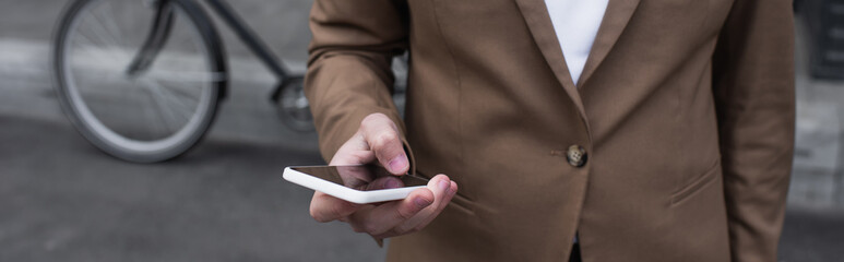 cropped view of young businessman in formal wear using smartphone outside, banner.