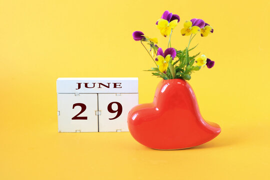 Calendar for June 29 : the name of the month of June in English, the number 29 on cubes, a vase in the shape of a red heart with a bouquet of violets on a yellow background