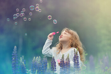 little blonde girl with curly hair walking in a field with lupins, blowing soap bubbles, summer...
