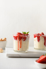 Layered summer dessert with strawberries, cookie savoyardi, mascarpone and whipped cream. Vertical orientation. Close up. Italian tiramisu with summer vibes on white.