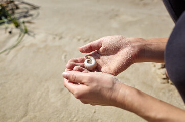 Female hands holds a seashell against the background of sand. Woman enjoying summer vacation