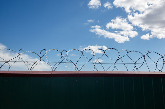 Metal wall with barbed wire against the blue sky background. Fence with barbwire for protection, space for text