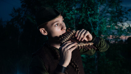 Peter Pan plays a flat sitting in the grass against the backdrop of the forest. Cosplay on Peter Foam. Robin Hood