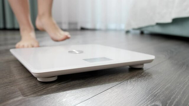 Closeup of bare female feet standing on digital scales on wooden floor at bedroom. Concept of dieting, loosing weight and healthy lifestyle.