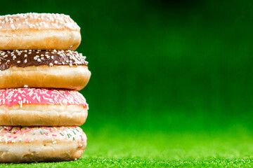 Mix of multicolored sweet donuts with sprinkel on green background