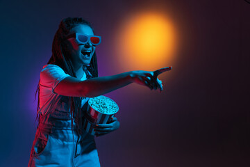 Excited in 3D eyewear and with popcorn. Caucasian woman's portrait isolated on blue studio background in pink neon light. Beautiful male model.