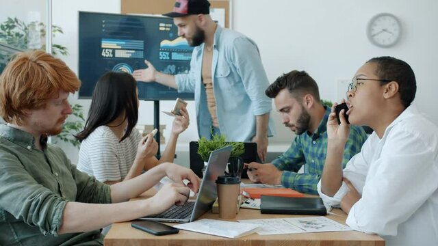 Unmotivated employees are ignoring business meeting and boss chatting on mobile phones and playing games having fun while manager is making presentation asking for attention