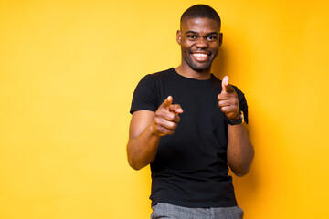 Handsome young african american guy in a black t-shirt points his finger at the camera and raises...