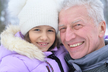 grandfather with granddaughter smiling, posing outdoors in winter