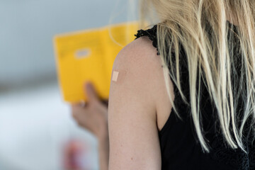 Junge Frau mit Pflaster auf dem Arm hält Impfausweis in der Hand,  nach Impfung gegen Covid19
