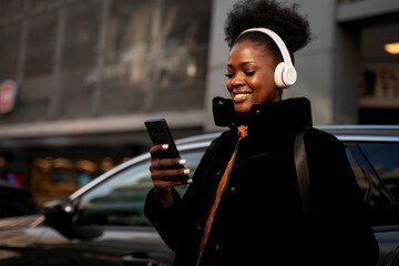 Young african woman outdoors. Beautiful woman listening to music while walking through the city.