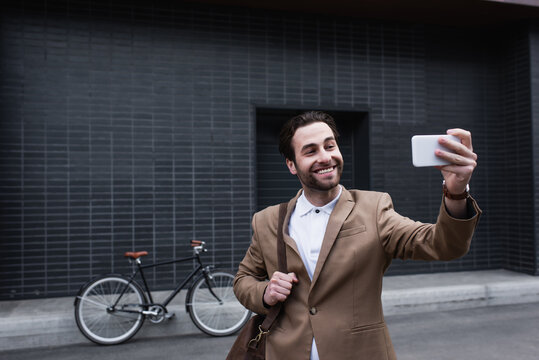 happy young businessman in formal wear taking selfie on cellphone outside.