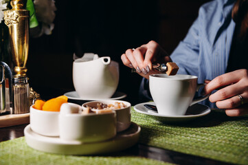 A woman with a cup of hot tea in her hands sits in the restaurant. The girl drinks aromatic tea. Enjoy the moment, take a break.