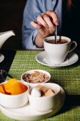 A woman with a cup of hot tea in her hands sits in the restaurant. The girl drinks aromatic tea. Enjoy the moment, take a break.