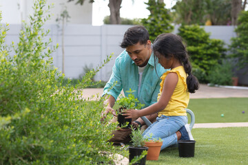 Smiling hispanic father and daughter gardening, kneeling and planting in flower bed