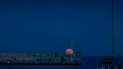 Obraz premium Roter Vollmond über dem Wasser in Hafenanlage