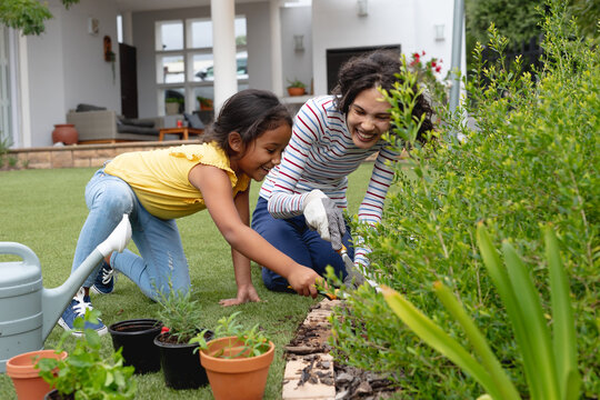 Smiling hispanic mother and daughter gardening, kneeling and planting in flower bed