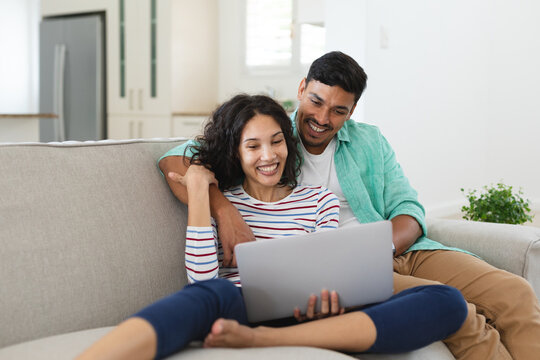Smiling hispanic couple sitting on couch using laptop together