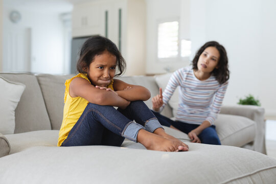 Sad hispanic daughter sitting on couch being told off by mother