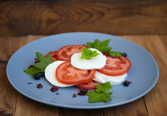Italian caprese salad with sliced tomatoes, mozzarella, basil, olive oil on a wooden background.