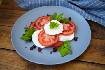 Italian caprese salad with sliced tomatoes, mozzarella, basil, olive oil on a wooden background.