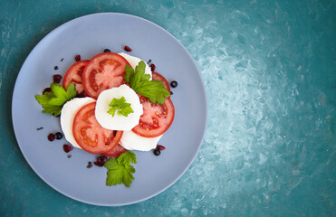 Italian caprese salad with sliced tomatoes, mozzarella, basil, olive oil on a blank plate. View from above.