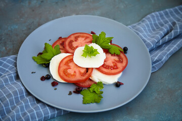 Italian caprese salad with sliced tomatoes, mozzarella, basil, olive oil on a blank plate. View from above.