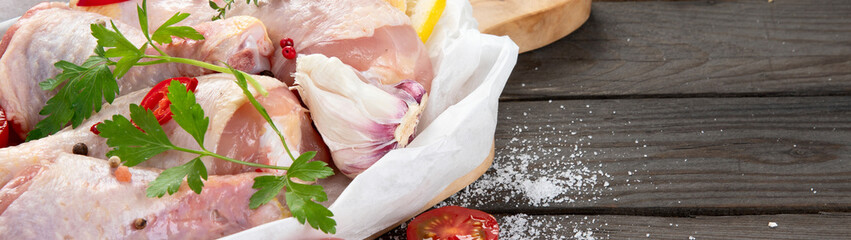 Raw chicken legs with spices and herbs for cooking on wooden background.