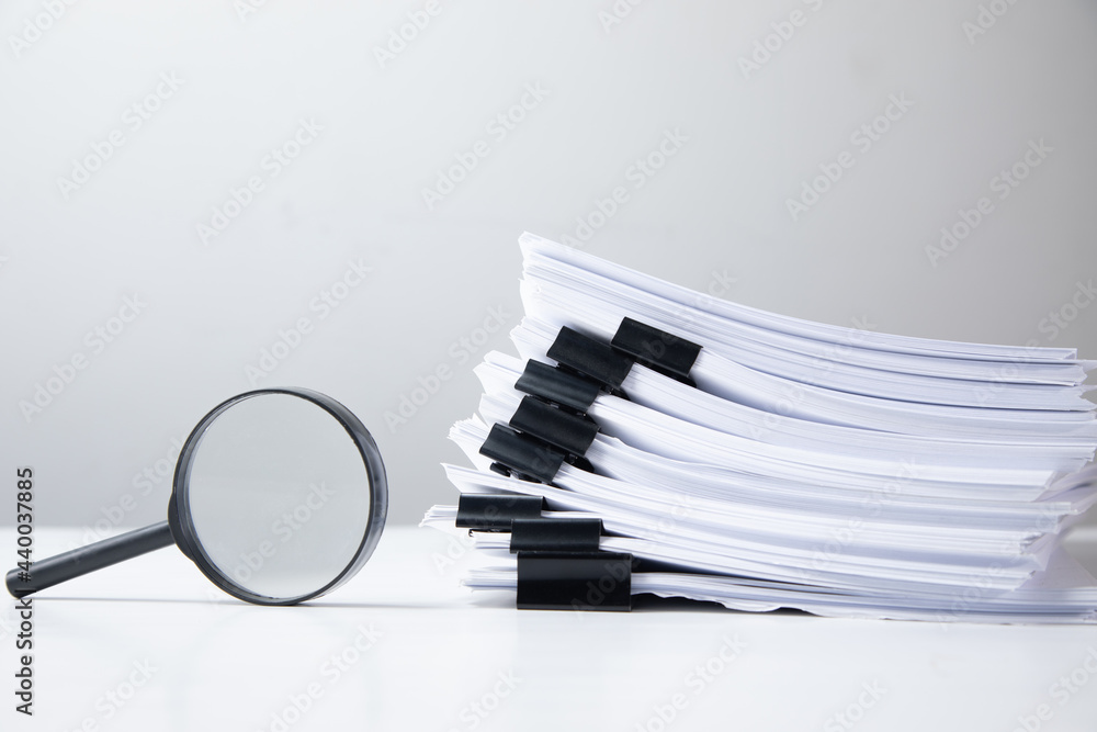 Poster stack of report paper documents with magnifying glass.