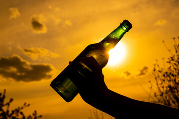 Woman holding bottle of beer outdoors against sky background.