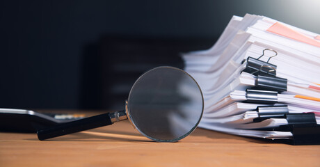 Stack of report paper documents with magnifying glass.