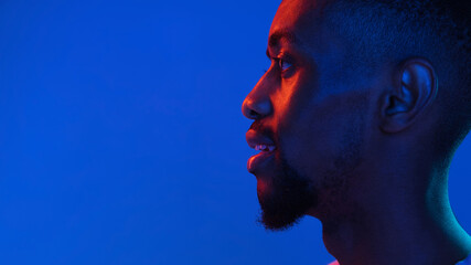 African-american young man's portrait on dark studio background in neon. Concept of human emotions,...