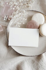 Sheet card mockup , wedding invitation, macaroons, perfume, white flowers on beige linen background. Copy space. Scandinavian life  style.