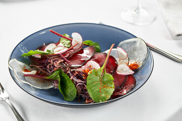Light appetizer bresaola with lettuce, Italian bresaola beef jerky on a light plate, close-up, copy...