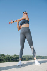 Upward photo of a confident young woman doing her stretches. Over blue sky