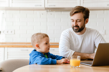 White father and son using laptop while sitting at table in kitchen